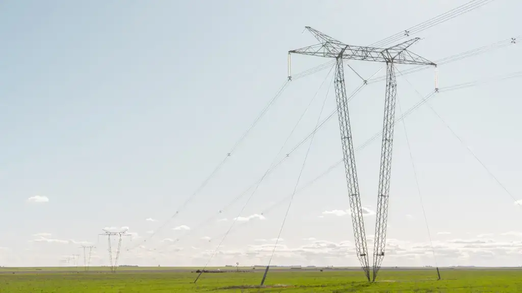 High-voltage transmission towers carrying power lines across open farmland under a clear sky